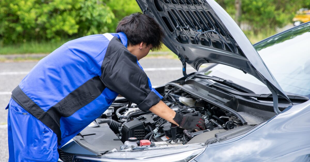 車のボンネットを開けてエンジンを点検する整備士