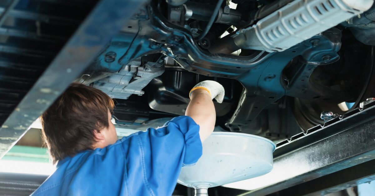 リフトアップされた車の下でオイル交換作業をする整備士