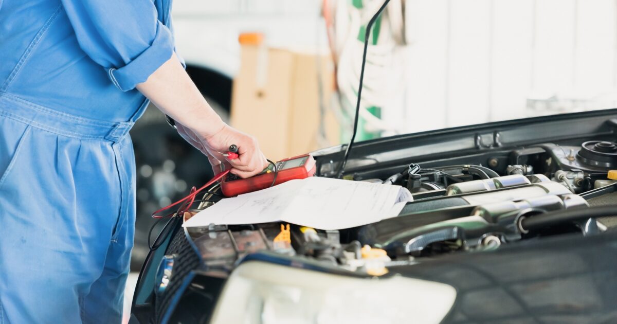 テスターで車の電圧を測定する整備士